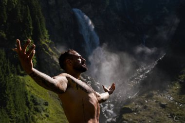 İnsan meditasyonu ve doğadaki refah. Çevrede özgürlük. Ormanda şelaleye karşı meditasyon yapan rahat bir adam. Özgürlük ve mutluluk yaşam tarzı. Sağlık kaplıcası, tatil ve yoga meditasyonu