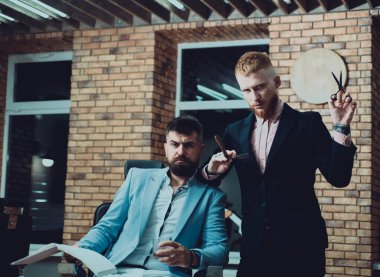 Making haircut look perfect in barbershop. Barber making haircut of attractive bearded man in barber shop. Barber shaving a bearded man in a barbershop. Balm on dry body parts to moisturize skin clipart