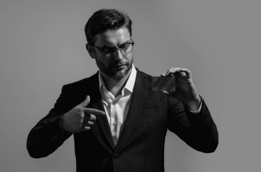Kredi kartıyla. Beyaz ırkın başarılı 40 'lı yılların iş adamı, bankacılık kartını gri arka planda, stüdyo portresi üzerinde izole bir şekilde tutuyor. İnsanların yaşam tarzı konsepti. Satın alma ve geri ödeme ödülleri