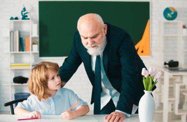 Öğretmen ve okul çocuğu. İlköğretim öğrencisi sınıfta öğretmenle birlikte okuyor ve yazıyor.