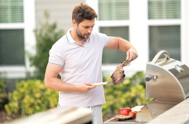 Evin arka bahçesinde mangalda et pişiren bir adam. Yakışıklı adam barbekü hazırlıyor. Barbekü şefi. Pişirme lezzetli ızgara ızgara yemek, bbq eti. Izgara ve barbekü.