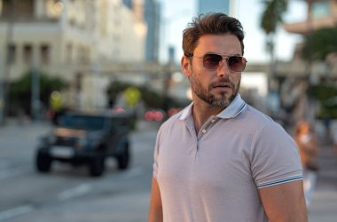 Şehir merkezinde sıradan, yakışıklı bir manken. İyi giyimli, gözlüklü ve polo pozu veren bir adam. Erkek model. Şehirde şık bir adamın portresi. Açık hava moda portresi