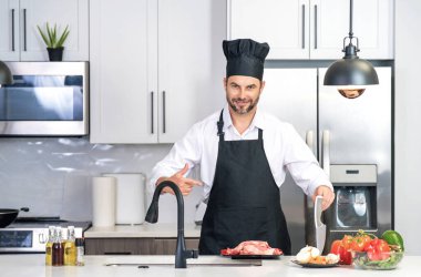 Yakışıklı adam mutfakta yemek hazırlıyor. Yakışıklı, orta yaşlı bir adam mutfakta et pişiriyor. Adam mutfakta yemek hazırlıyor. Mutfak konseptinde sağlıklı yemek ve yemek.