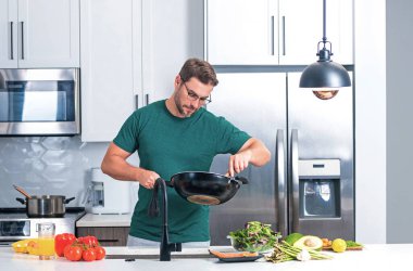 Evde yemek pişirmek. Mutfakta yemek hazırlayan adam. Erkek aşçı evde yemek hazırlıyor. Şef yemek yapıyor. Yemek pişiren adam, mutfak tenceresi, yemek tabağı. Adam mutfak içinde çorba hazırlıyor.