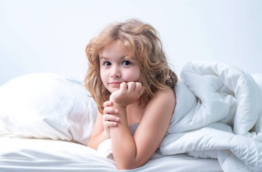 Çocuk sabah yatak odasında uyanır. Sevimli küçük çocuk yatakta uyanıyor.