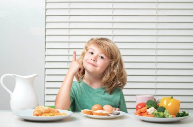 Okul çocuğu okuldan önce kahvaltı yapıyor. Küçük bir çocuğun portresi. Mutfaktaki masada oturuyor. Lezzetli, besleyici bir kahvaltı yapıyor.