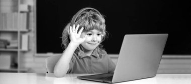 Kulaklıklı mutlu çocuk okulda bilgisayarda video dersi izliyor, kulaklıklı çocuk internette bilgisayar kullanıyor.