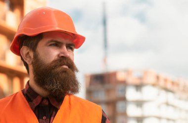 İnşaatçının portresi. Miğferli işçi inşaat alanında poz veriyor.