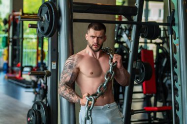Ağırlık metal zincirlerle egzersiz yapan bir adam. Uygun model ağırlık kaldırma zinciri, spor salonunda egzersiz. Zincirlerle çalış. Güçlü, kaslı, formda, zincirleri ve ağır ağırlığı olan bir adam. Pazılar için alıştırmalar
