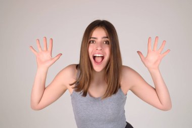 Kaşlarını kaldıran kız şaşırıyor ve şok oluyor. Beklenmedik haberlere şaşırmış bir tepki. Stüdyoda izole edilmiş tişörtlü bir kız. Yüzünde şok, şaşkınlık ve şaşkınlık ifadesi var.