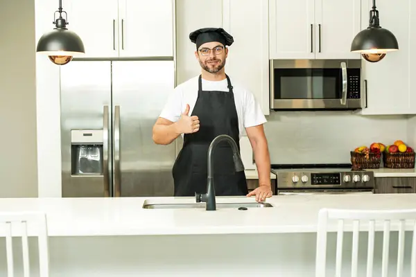 stock image Happy baker with thumb up. Portrait of chef man in a chef cap in the kitchen. Man wearing apron and chefs uniform and chefs hat. Character kitchener, chef for advertising