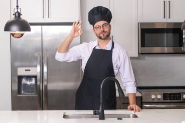 Tamam işareti olan bir aşçı, lezzetli yemekler. Aşçılık ve aşçılık. Restoran menüsü konsepti. Yemek servisi, yemek pişirme, yemek reklamcılığı. Üniformalı adam mutfakta.