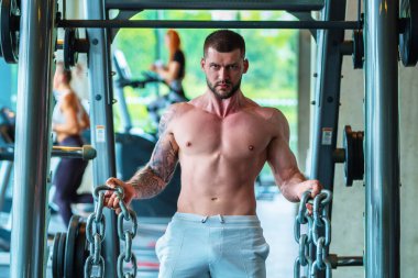 Kas yığını adam spor salonunda dambıllarla antrenman yapıyor. Spor salonunda poz veren kaslı yakışıklı bir adam. Kas sporcusu dambılı kaldırıyor. Spor kulübünde esneme, spor egzersizleri.