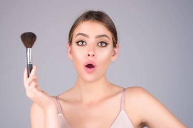 Studio portrait of a woman applying cosmetic tonal foundation on face using makeup brush. Beautiful girl doing contouring apply blush on cheeks isolated on studio background