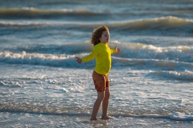 Mutlu çocuk yaz denizinde su sıçratarak oynuyor. Yaz tatili. Çocuk denizde dalgalarla oynuyor. Küçük çocuk denizde oynuyor ve su damlaları sıçrıyor. Çocuk denizde su sıçratmaca oynuyor. Yaz tatili