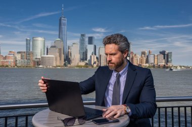 Başarılı ABD 'li işadamı. New York 'ta dizüstü bilgisayar kullanan bir adam. İş başarısı. Amerikan iş rüyası. Manhattan yakınlarında takım elbiseli Amerikalı iş adamları. ABD 'de online iş