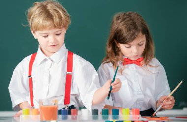 Sınıfta karatahta arka planda komik öğrenciler çiziyor. Okul arkadaşları çocuklar erkek ve kız birlikte resim yapıyorlar.