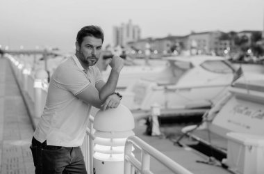 Şehirde kendine güvenen yakışıklı bir adamın portresi. Modern büyük Amerikan şehrinde kendine güvenen bir adamın portresi. Şık bir Lambersex modeli. Polo giymiş seksi bir adam. Yatın yanında zengin bir adam hayal ediyor.