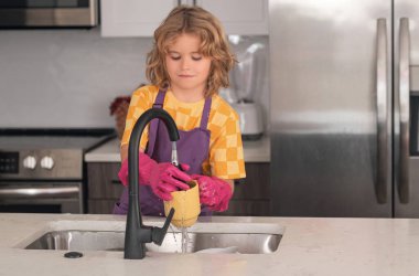 Sevimli çocuk mutfakta bulaşık yıkamaya yardım ediyor. Kithen 'ı temizleyen çocuk ev işlerine yardım ediyor. Tatlı çocuk temizliği, çocuk temizliği.