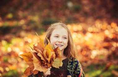 Sonbahar parkında gülümsüyor ve eğleniyor. Parktaki sevimli küçük kız. Güneşli bir sonbahar gününde güzel bir sonbahar parkında oynayan mutlu küçük kız. Güzel bir sonbahar gününde sevimli bir kız portresi.