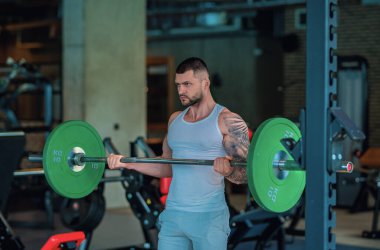 Kas yığını adam spor salonunda dambıllarla antrenman yapıyor. Spor salonunda poz veren kaslı yakışıklı bir adam. Kas sporcusu dambılı kaldırıyor. Spor kulübünde esneme, spor egzersizleri.
