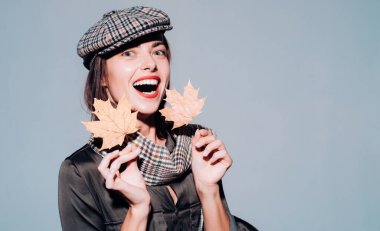 Altın yaprak ile mevsimlik giysiler içinde çekici genç kadın. Yaprakları ile oynama ve kameraya arıyorum sürpriz kadın. Sonbahar ruh hali ve hava sıcak ve güneşli ve yağmur mümkündür