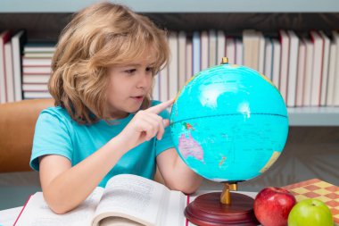 Pupil looking at globe in library at the elementary school. Back to school. Portrait of cute child school boy. Clever kid with school supplies