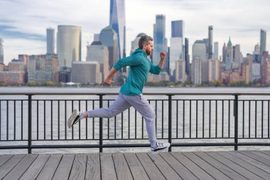 New York 'ta spor kıyafeti giyen bir koşucu. Hareket, sağlıklı koşu. Manhattan yakınlarında koşan bir koşucu. Kaslı sporcu şehirde koşuyor. Spor kıyafetleri. Dışarıda antrenman yapan yakışıklı adam.