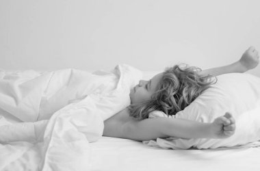 Çocuk uyanıyor ve elini kaldırıyor. Yatağında rahat, yumuşak yastık bezi olan bir çocuk. Çocuk battaniyeyi kaldırdı. Günaydın.