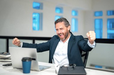 Ofisinde dizüstü bilgisayarı olan bir iş adamı. Modern ofiste çalışan uzaktan kumandalı personel. İş adamı çevrimiçi toplantıda. İnternette çalışan İspanyol iş adamı. İş yerinde dizüstü bilgisayar kullanan heyecanlı bir iş adamı