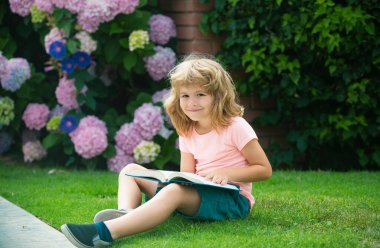 Çocuk bahçede faiz kitabı okuyor. Yaz eğlencesi. Çimlerin üzerinde oturup çocuk kitabı okuyan tatlı bir çocuk. Öğrenme kavramı