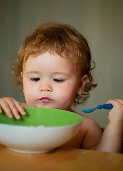 stock image Portrait of funny little baby boy eating from plate holding spoon closeup