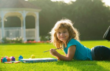 Çocuklar ressamlar yaratıcılık tatilini resmediyor. Çocuklar parkın dışında boya renginde ve fırçayla resim yapıyorlar.