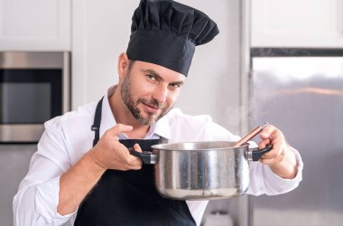 Aşçı adam mutfakta tencerede yemek pişiriyor. Gurme yemeği hazırlama süreci. Adam evde yemek pişiriyor, esrar kullanıyor. Şef yemek pişiriyor. Yakışıklı aşçı aşçı konsepti