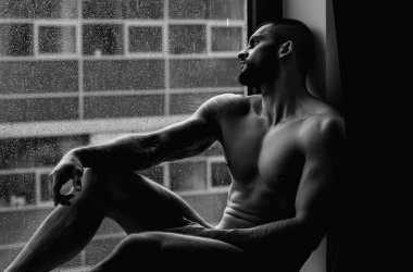 Muscular male torso, bare shoulders. Nude man in a bedroom. Young sexy body of strong man at morning. Muscular man in hotel room on window curtains. Shirtless topless sexy male model posing indoor