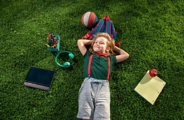 Doğadaki okul çocuğu. Okul malzemesi taşıyan inek öğrenci. Çocuk çimlerin üzerinde yatıyor. Rüyamda ders çalışıyordum. Yeşil çimlerin üzerinde uzanan küçük bir çocuk manzarası