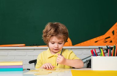Karatahta masasının yanındaki sınıfta tatlı bir çocuk. Öğretmenler günü. Eğitimsel süreç. Okuldaki küçük çocuklar.
