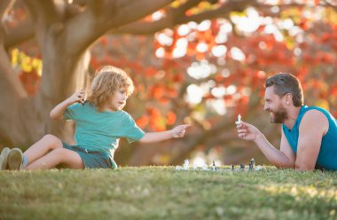 Baba ve çocuk çim parkında çimlerde satranç oynuyorlar. Babalar Günü, aileyi sevmek, ebeveynlik, çocukluk kavramı.