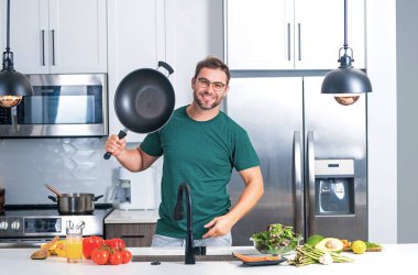 Aşçı mutfakta tavayla yemek pişiriyor. Şef aşçı tavayla hazırlar. Aşçı modern mutfakta tavayla yemek pişiriyor. Olgun aşçı adam mutfakta durup yemek hazırlıyor.