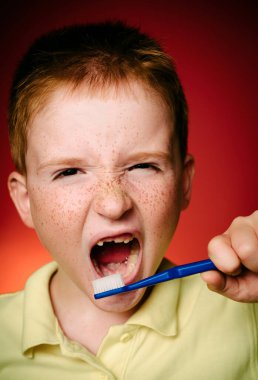 Çocuk temiz dişler diş fırçası ile. Gömlek tasarım, sağlık, ağız hijyeni. Diş fırçası izole kırmızı zemin üzerine el ile boy gülümseyerek. Mutlu küçük çocuk dişlerini fırçalıyor