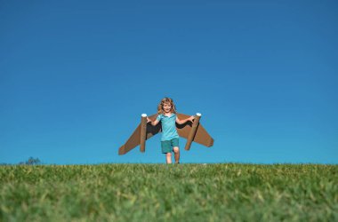 Parkta oynayan mutlu çocuk. Oyuncak kağıt kanatlarla eğlenen bir çocuk. Pilot olmayı hayal eden küçük bir çocuk. Gökyüzü mavisi arka planda kopya alanı olan komik bir çocuk.