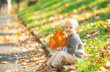 Sonbahar yapraklarıyla oynayan tatlı bir çocuk. Sonbahar doğa arka planında kalın ceketli şirin bir çocuk. Mutlu çocuk sonbaharda dışarıda rüya görür. Rüya gören çocuklar.
