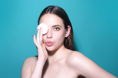 Removing makeup with cotton pads. Cleaning face with pad. Cosmetic cotton pad. Young woman caring for facial skin using cotton pad in studio. Beauty care and pampering. Daily skincare