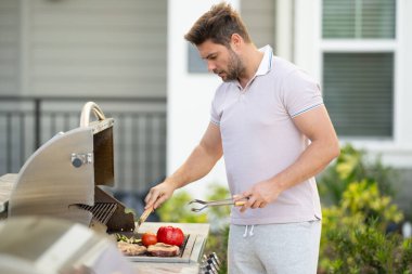 Yakışıklı adam barbekü hazırlıyor. Erkek aşçı ızgarada et pişiriyor. Evin arka bahçesinde yaz yemeği için barbeküde et pişiren adam.