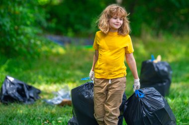 Çevre plastik kirliliği. Ormanda çöp toplayan ve elinde çöp torbası tutan gönüllü bir çocuk. Çevresel koruma. Çevre aktivisti. Çevre koruma ve atık kirliliği