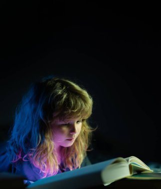 Çocuk karanlık odada masal okuyor. Küçük bir çocuk karanlık evde kitap okuyor. Çocuklar gece lambasıyla yüz yüze