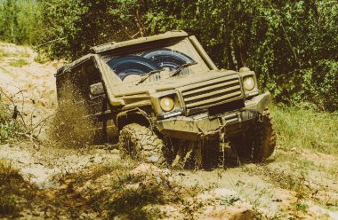 Dağların arasında bir kamyonet. 4x4 yolculuk gezisi. Jeep su birikintisine çarptı ve toprak püskürttü. Aşağıdan büyük off-road araba tekerleği kırsal yolda ve dağların gerisinde