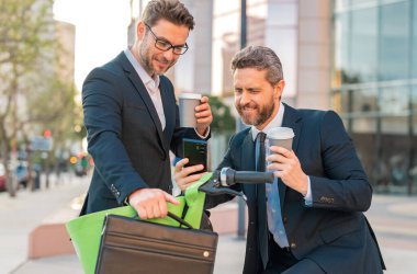 Thoughtful businessman wearing a suit front of office outdoor. Business man standing in front of city skyscraper. Two business men using phone outdoor clipart