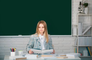 Sınava hazırlanan, elinde kitap tutan bir üniversite öğrencisi. Karatahta arkaplanında fotokopi aletiyle kitap okuyan tatlı kız.