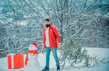 Komik Noel Baba balta ve Noel ağacı ile poz. Sakallı adam eve bir Noel ağacı taşır. Kış parkı Noel ağacı ile Adam keresteci